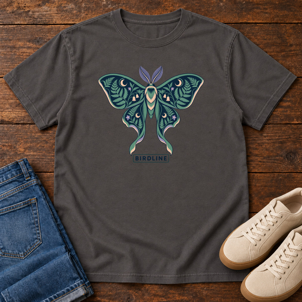 Botanical Moth T-Shirt in Graphite, front laid flat on wood, featuring a teal moth with patterned wings, leaves and crescent moons.