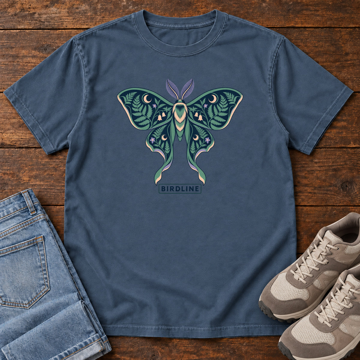 Botanical Moth T-Shirt in Midnight, front laid flat on wood, featuring a teal moth with patterned wings, leaves and crescent moons.