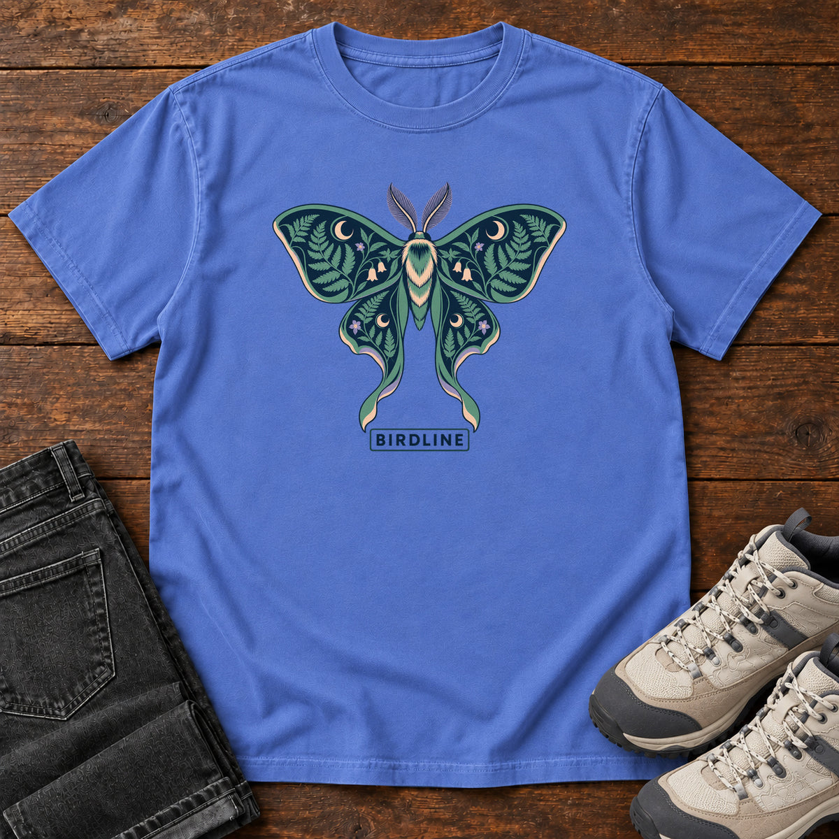 Botanical Moth T-Shirt in Mystic Blue, front laid flat on wood, featuring a teal moth with patterned wings, leaves and crescent moons.