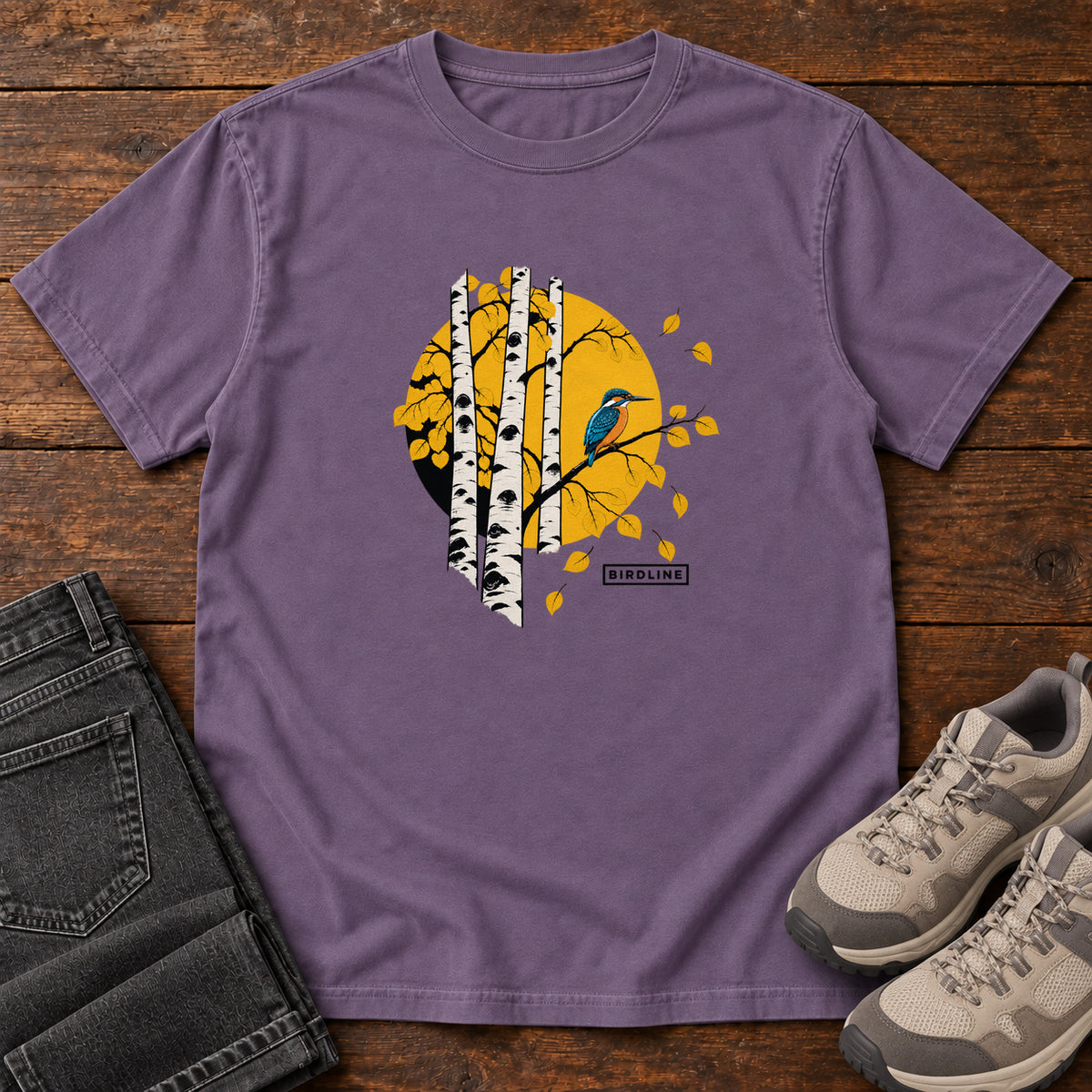 Grape Aspens Kingfisher T-Shirt with a blue bird perched among white tree trunks against a golden circle, front flat lay on wood.