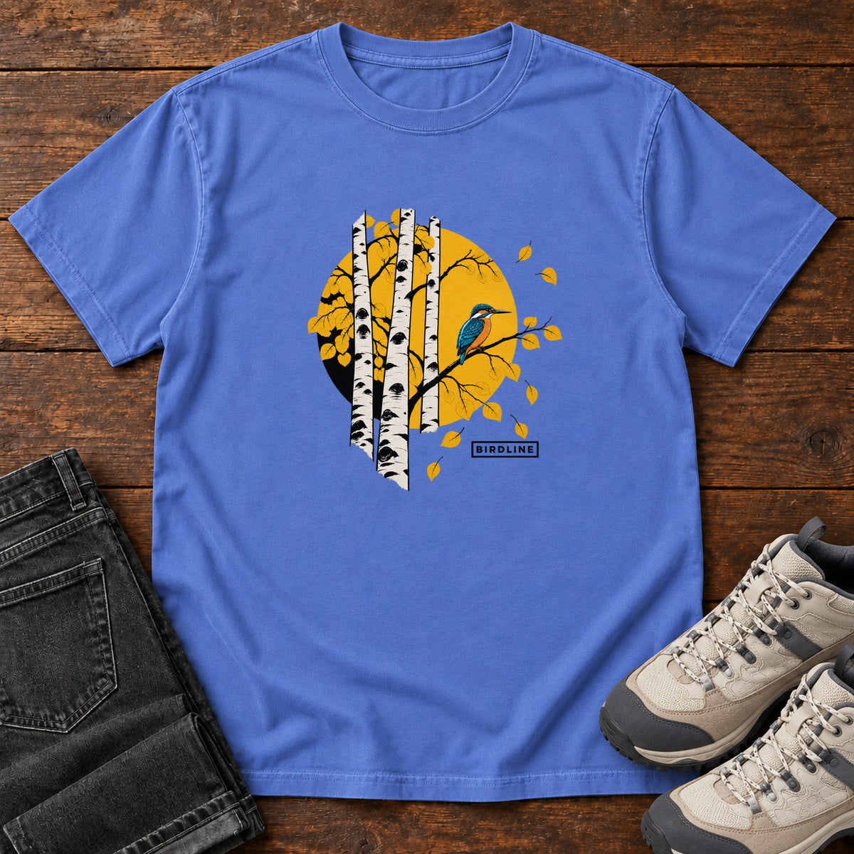 Mystic Blue Aspens Kingfisher T-Shirt with a blue bird perched among white tree trunks against a golden circle, front flat lay on wood.