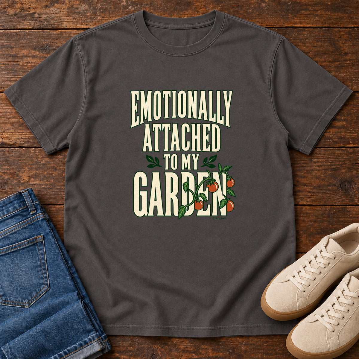 Graphite Emotionally Attached to My Garden T-Shirt with cream lettering intertwined with a leafy vine and orange fruit, front flat lay on wood.