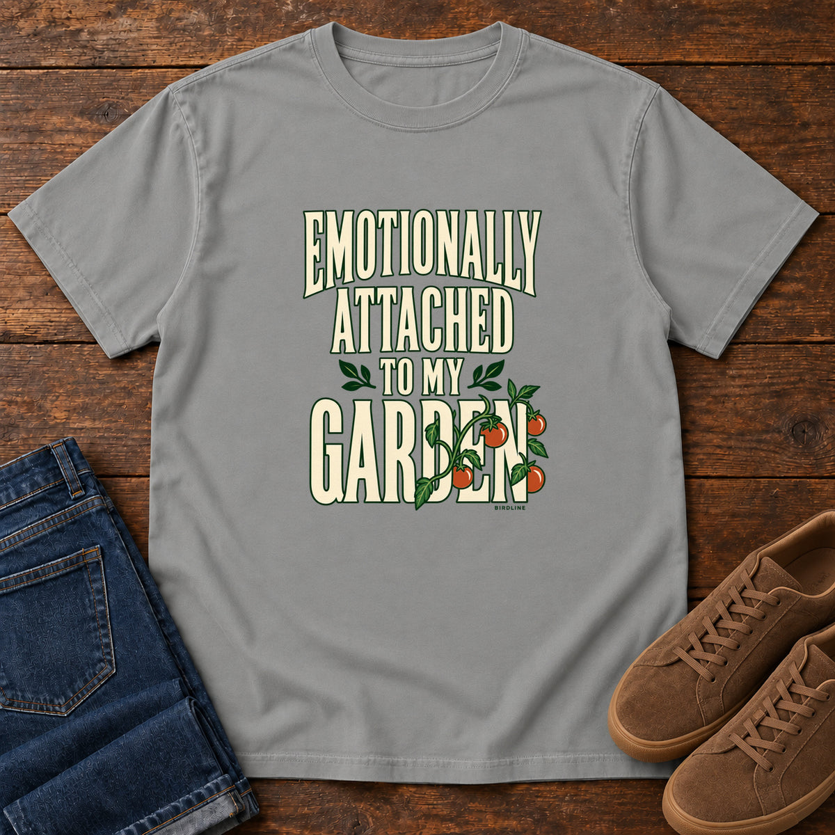 Grey Emotionally Attached to My Garden T-Shirt with cream lettering intertwined with a leafy vine and orange fruit, front flat lay on wood.
