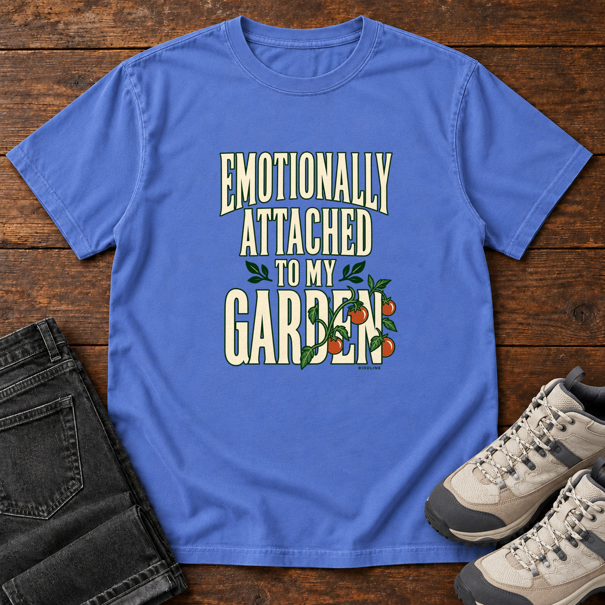 Mystic Blue Emotionally Attached to My Garden T-Shirt with cream lettering intertwined with a leafy vine and orange fruit, front flat lay on wood.