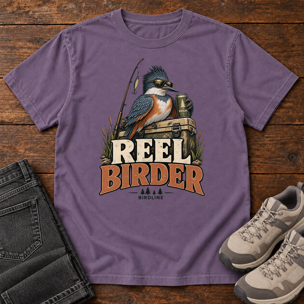 Grape Reel Birder T-Shirt with a crested bird in sunglasses holding a mug beside a fishing rod and tackle box; front flat lay on wood.