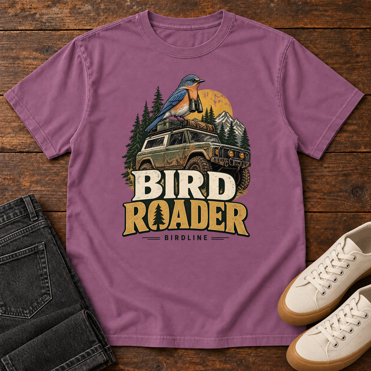 Bird Roader T-Shirt in Berry, front laid flat on wood, featuring a blue-and-orange bird above an off-road vehicle, pine trees, mountains and a yellow sun.
