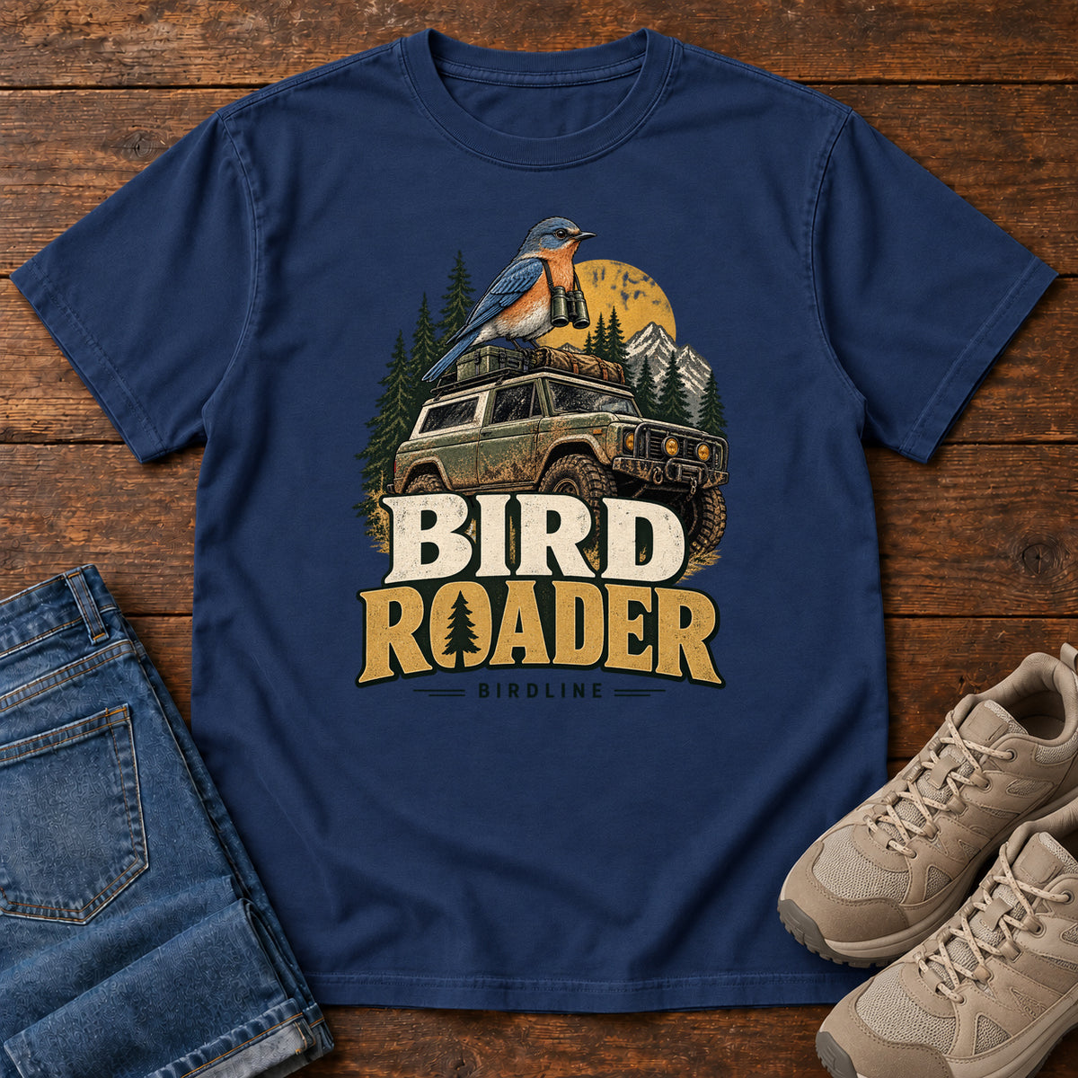 Bird Roader T-Shirt in True Navy, front laid flat on wood, featuring a blue-and-orange bird above an off-road vehicle, pine trees, mountains and a yellow sun.