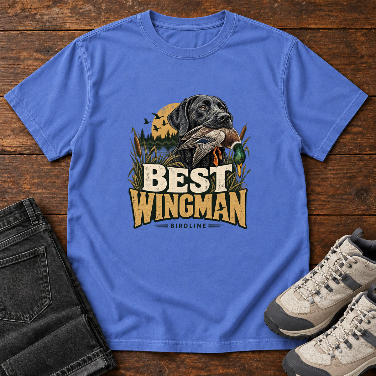 Mystic Blue Best Wingman T-Shirt with a black dog carrying a duck, marsh reeds and cream-and-gold lettering, front flat lay on wood.