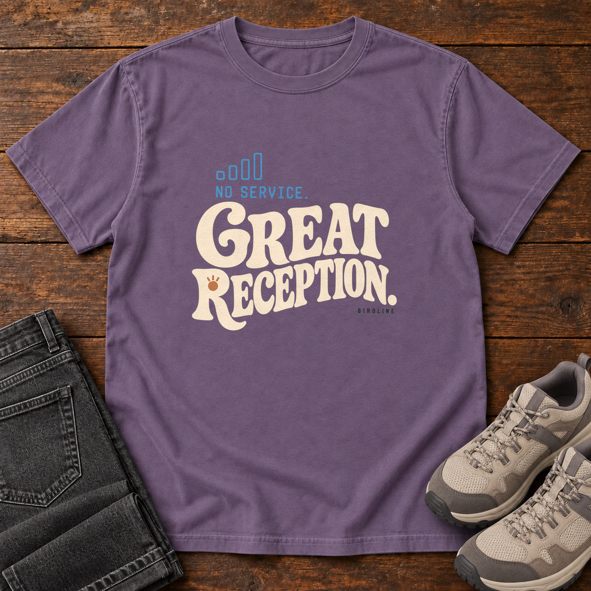 Grape No Service. Great Reception. T-Shirt with cream retro lettering and blue outlined phone-signal bars; front flat lay on wood.
