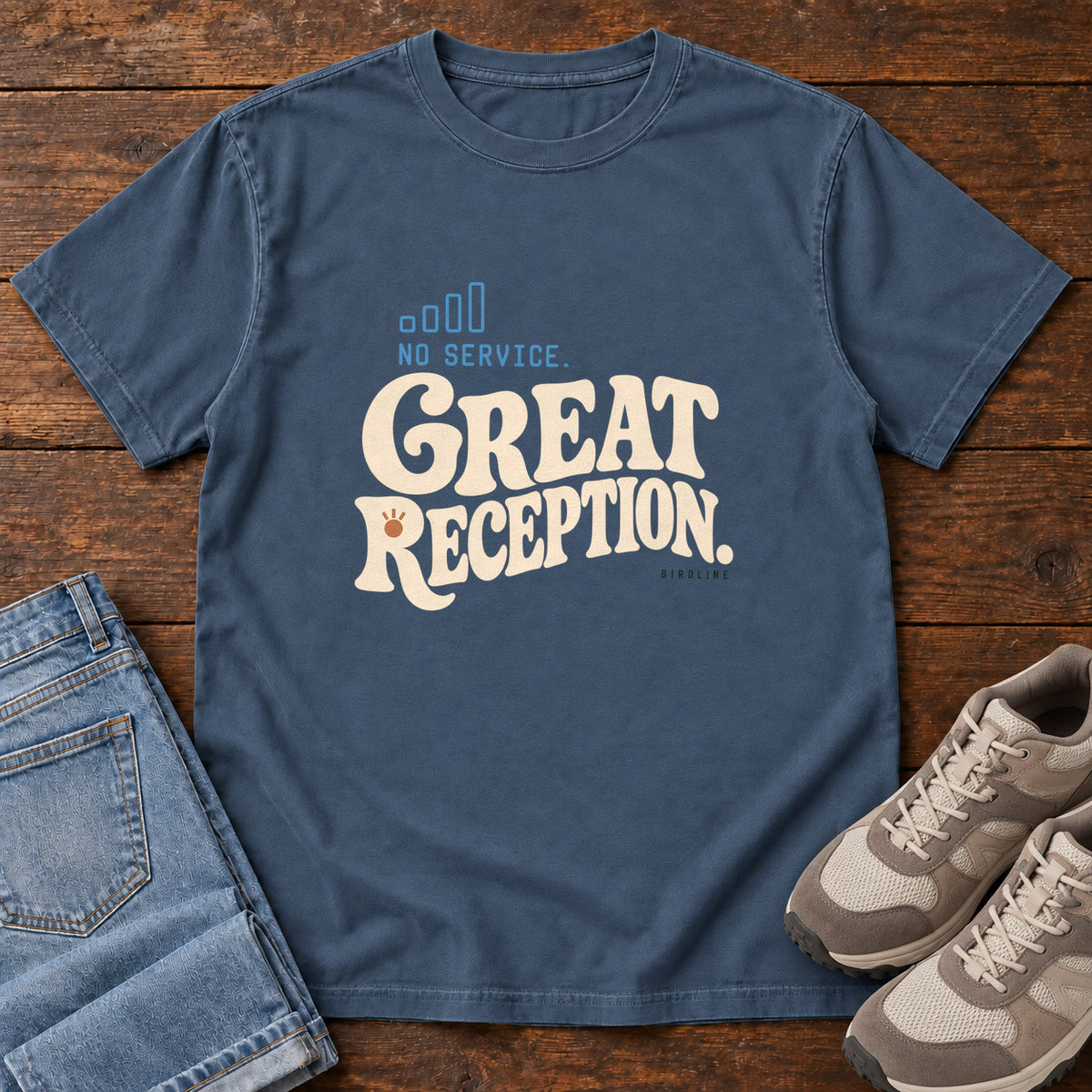 Midnight No Service. Great Reception. T-Shirt with cream retro lettering and blue outlined phone-signal bars; front flat lay on wood.