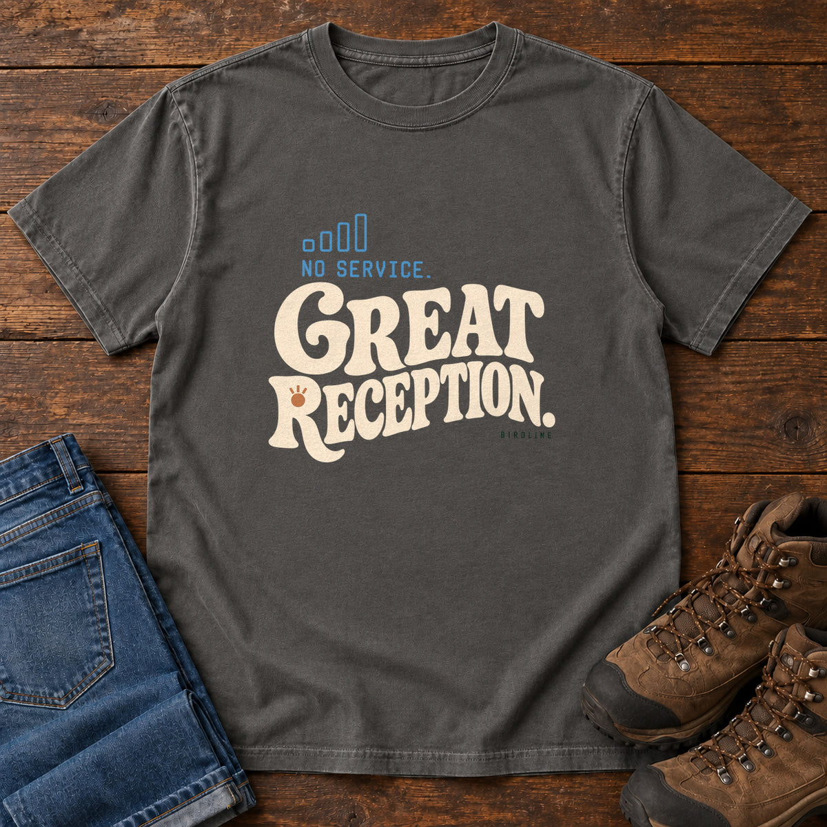 Pepper No Service. Great Reception. T-Shirt with cream retro lettering and blue outlined phone-signal bars; front flat lay on wood.