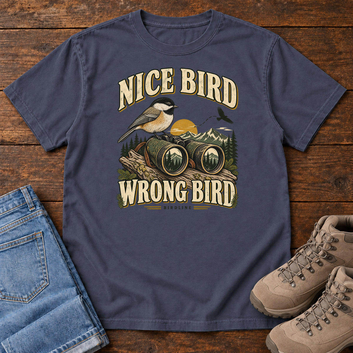 Navy Nice Bird. Wrong Bird. T-Shirt with a small black-capped bird on binoculars against mountains and a golden sun; front flat lay on wood.