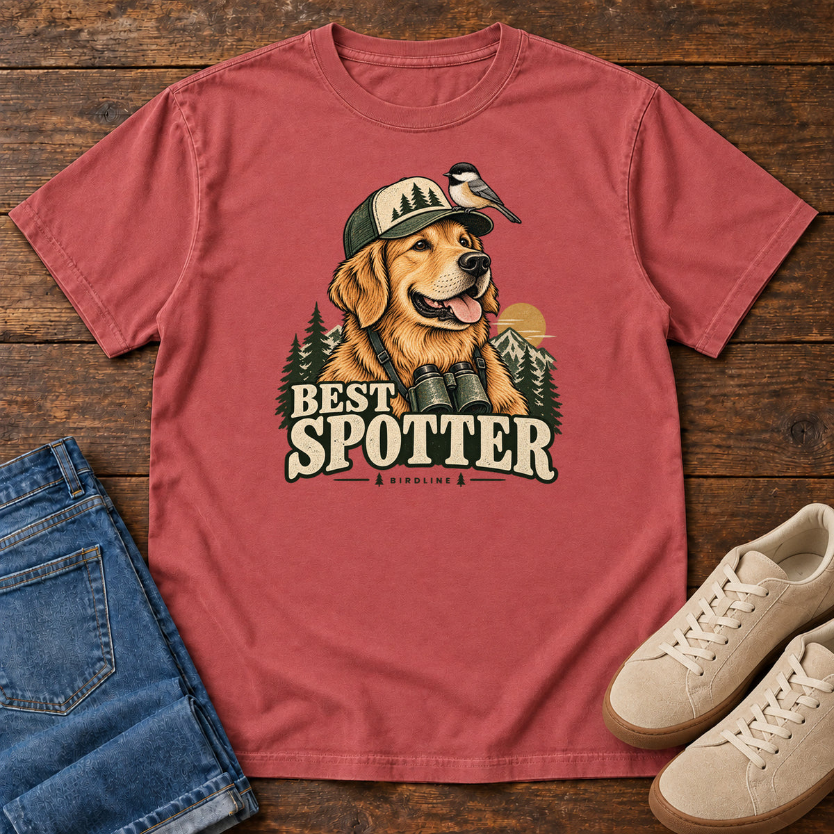 Crimson Best Spotter T-Shirt with a golden dog wearing a cap and binoculars, with a small bird perched on the cap, front flat lay on wood.