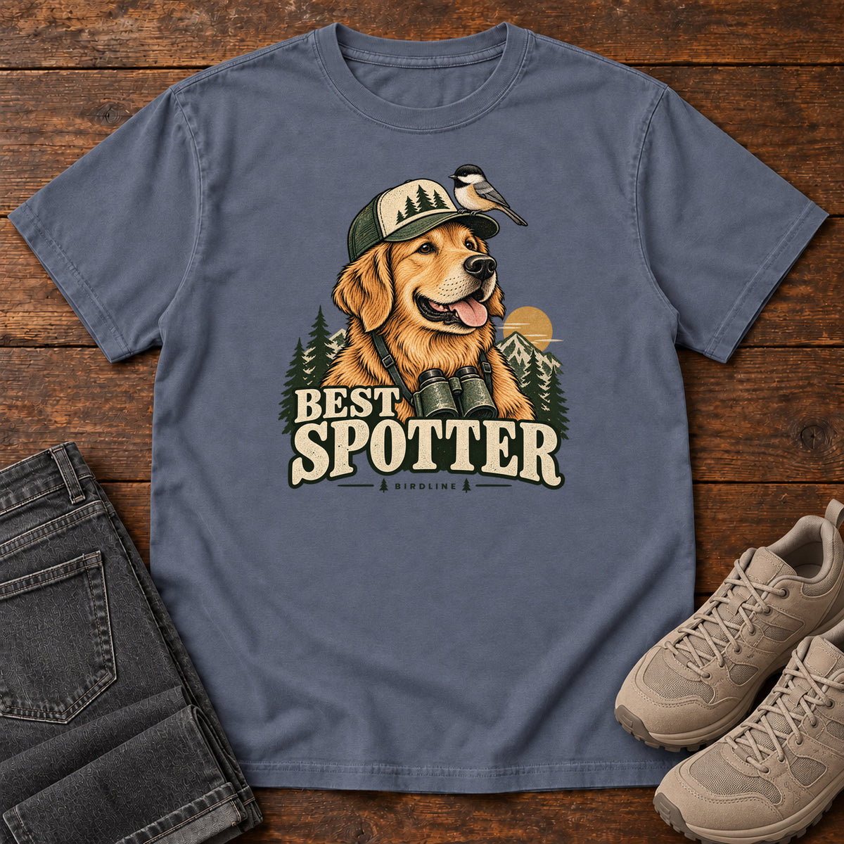 Denim Best Spotter T-Shirt with a golden dog wearing a cap and binoculars, with a small bird perched on the cap, front flat lay on wood.