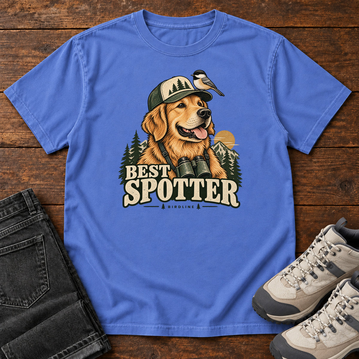 Mystic Blue Best Spotter T-Shirt with a golden dog wearing a cap and binoculars, with a small bird perched on the cap, front flat lay on wood.