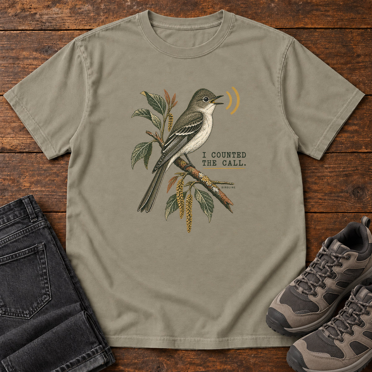 Sandstone I Counted the Call Songbird T-Shirt – Perched with a perched bird on a leafy branch and yellow sound-wave marks; front flat lay on wood.