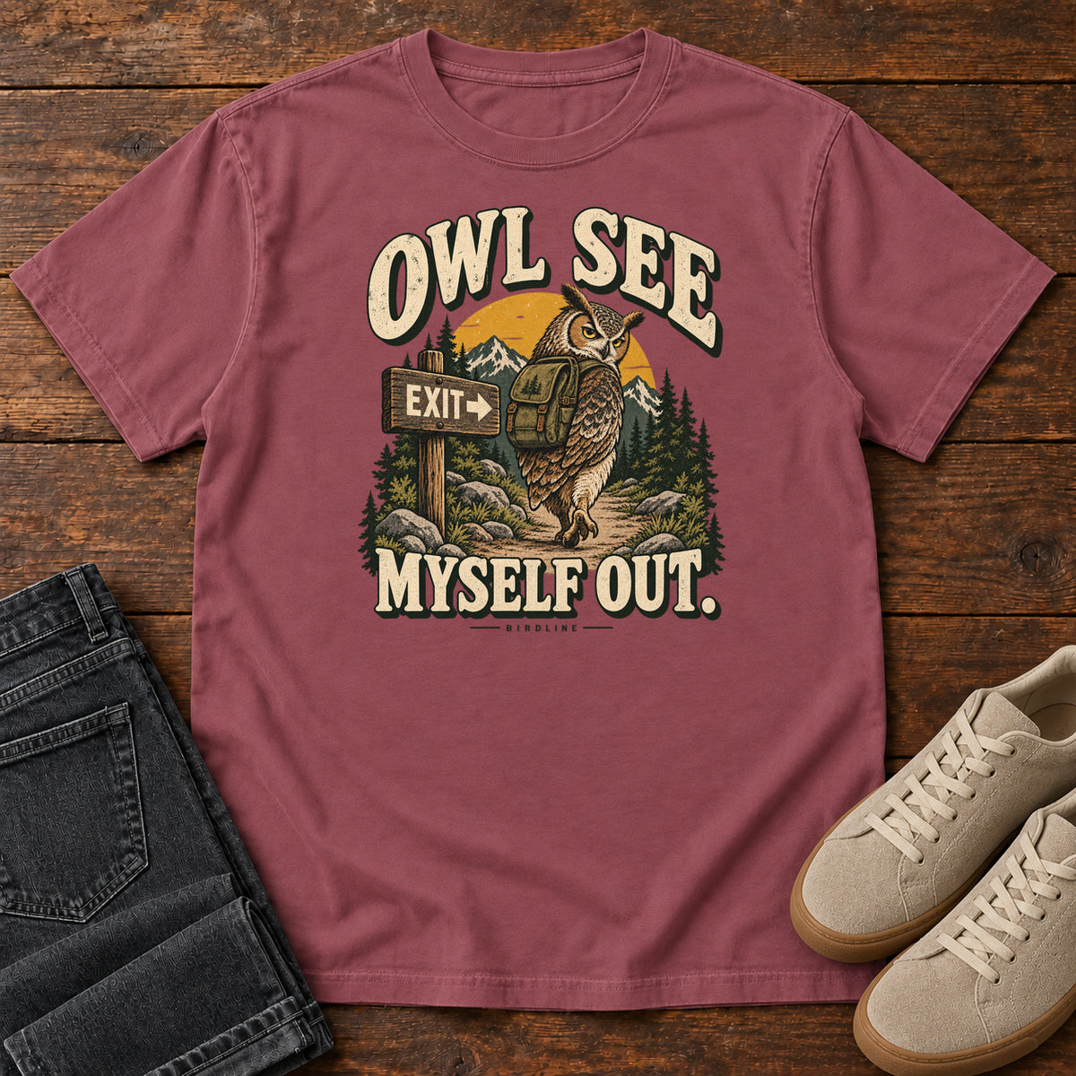 Brick Owl See Myself Out T-Shirt with an owl wearing a backpack beside an Exit sign on a woodland trail; front flat lay on wood.