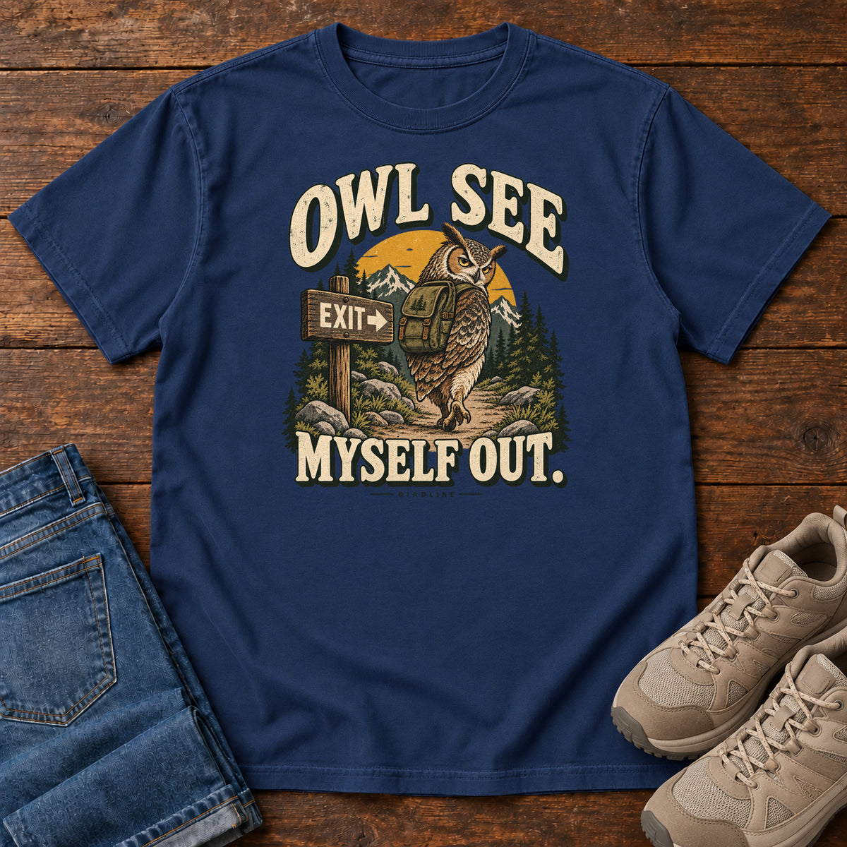 True Navy Owl See Myself Out T-Shirt with an owl wearing a backpack beside an Exit sign on a woodland trail; front flat lay on wood.