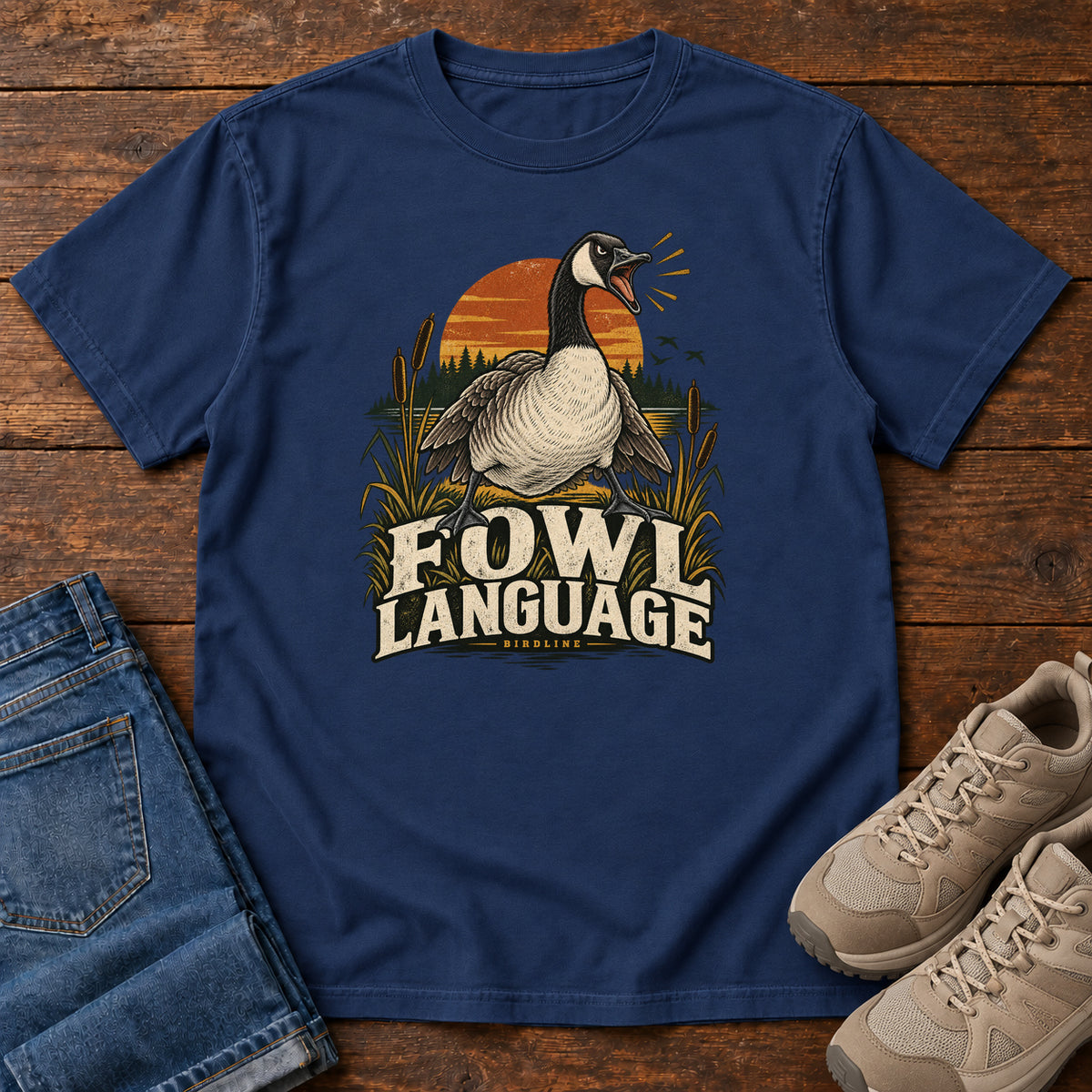 True Navy Fowl Language T-Shirt with an open-beaked goose among reeds against an orange sunset; front flat lay on wood.