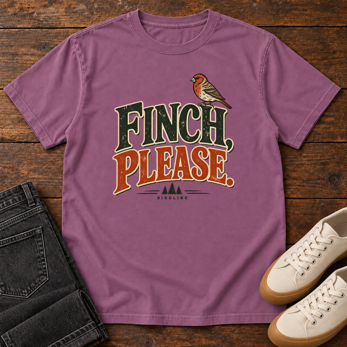 Berry Finch, Please. T-Shirt with a small bird perched above cream-outlined green-and-orange lettering, front flat lay on wood.