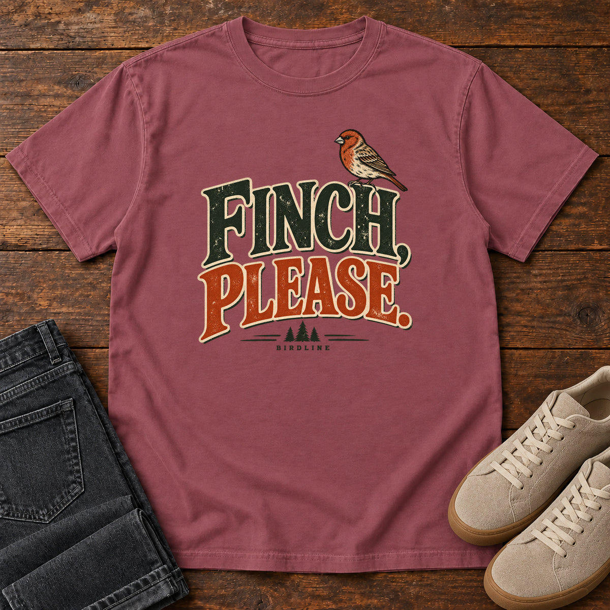 Brick Finch, Please. T-Shirt with a small bird perched above cream-outlined green-and-orange lettering, front flat lay on wood.