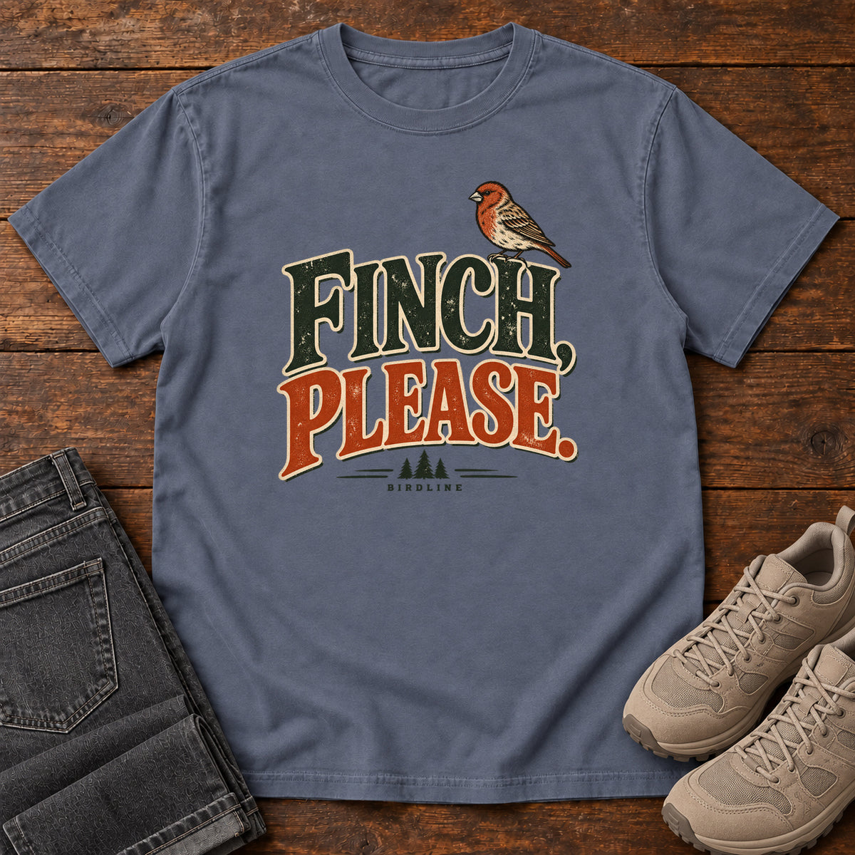 Denim Finch, Please. T-Shirt with a small bird perched above cream-outlined green-and-orange lettering, front flat lay on wood.