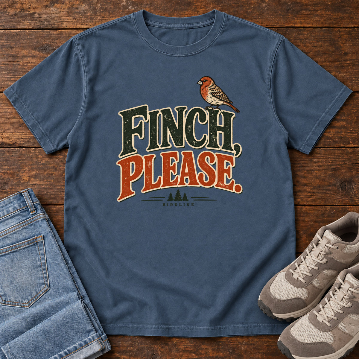 Midnight Finch, Please. T-Shirt with a small bird perched above cream-outlined green-and-orange lettering, front flat lay on wood.