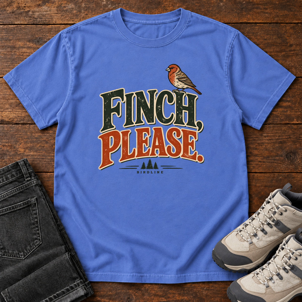 Mystic Blue Finch, Please. T-Shirt with a small bird perched above cream-outlined green-and-orange lettering, front flat lay on wood.