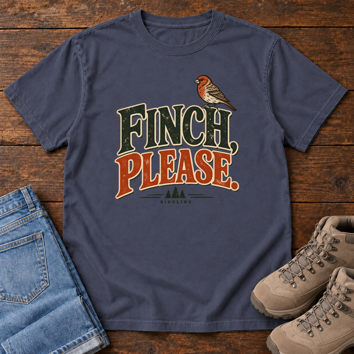 Navy Finch, Please. T-Shirt with a small bird perched above cream-outlined green-and-orange lettering, front flat lay on wood.