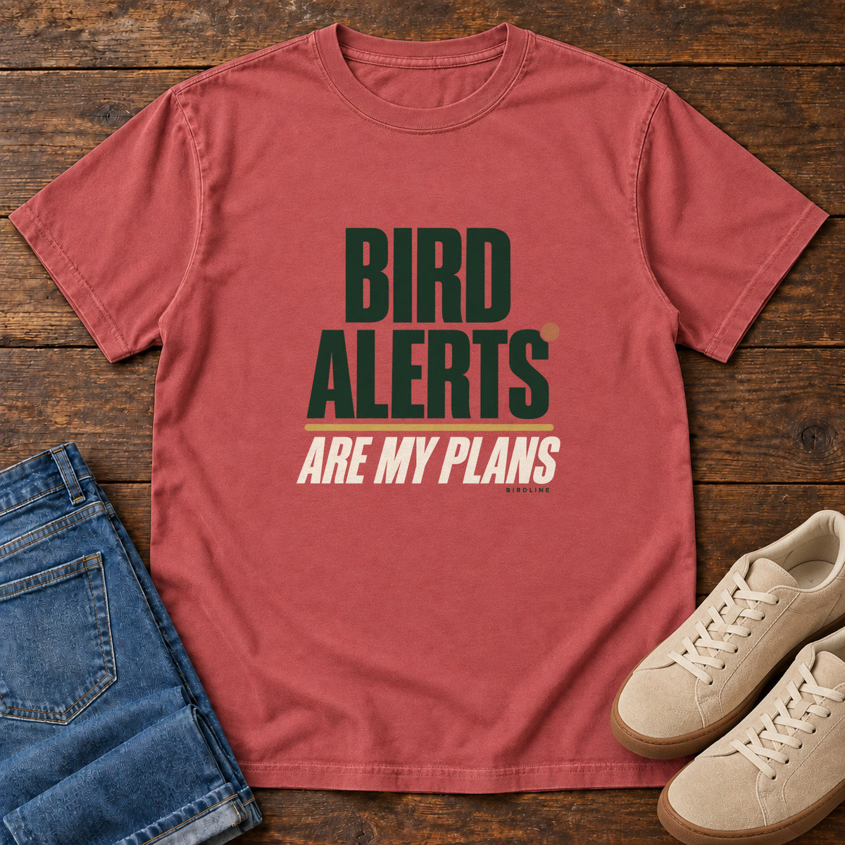 Crimson Bird Alerts Are My Plans T-Shirt with stacked green-and-cream lettering and an orange accent; front flat lay on wood.