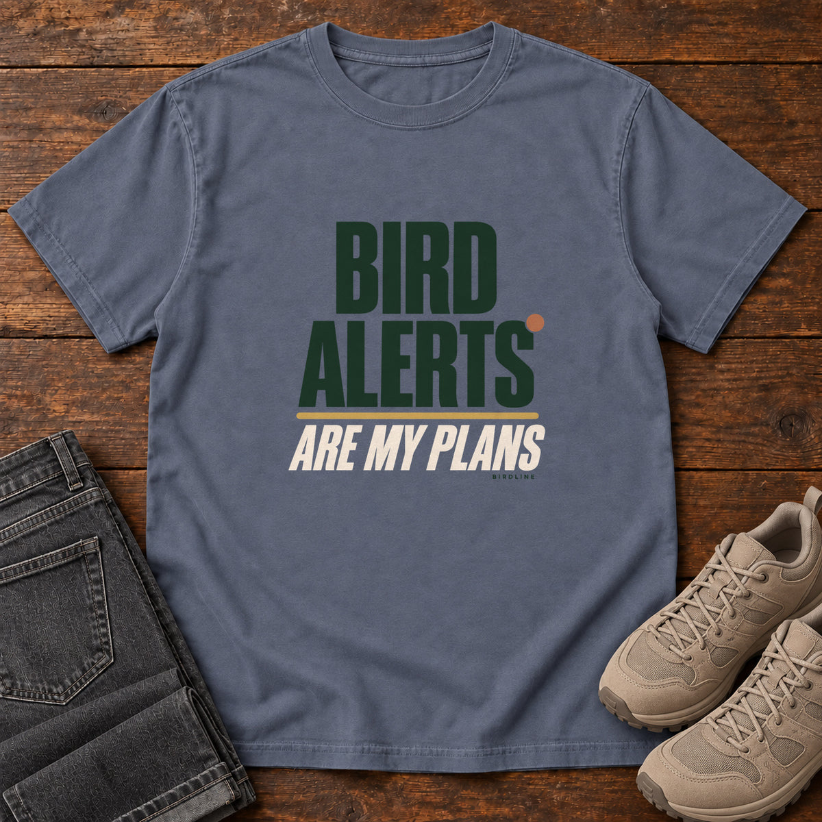 Denim Bird Alerts Are My Plans T-Shirt with stacked green-and-cream lettering and an orange accent; front flat lay on wood.