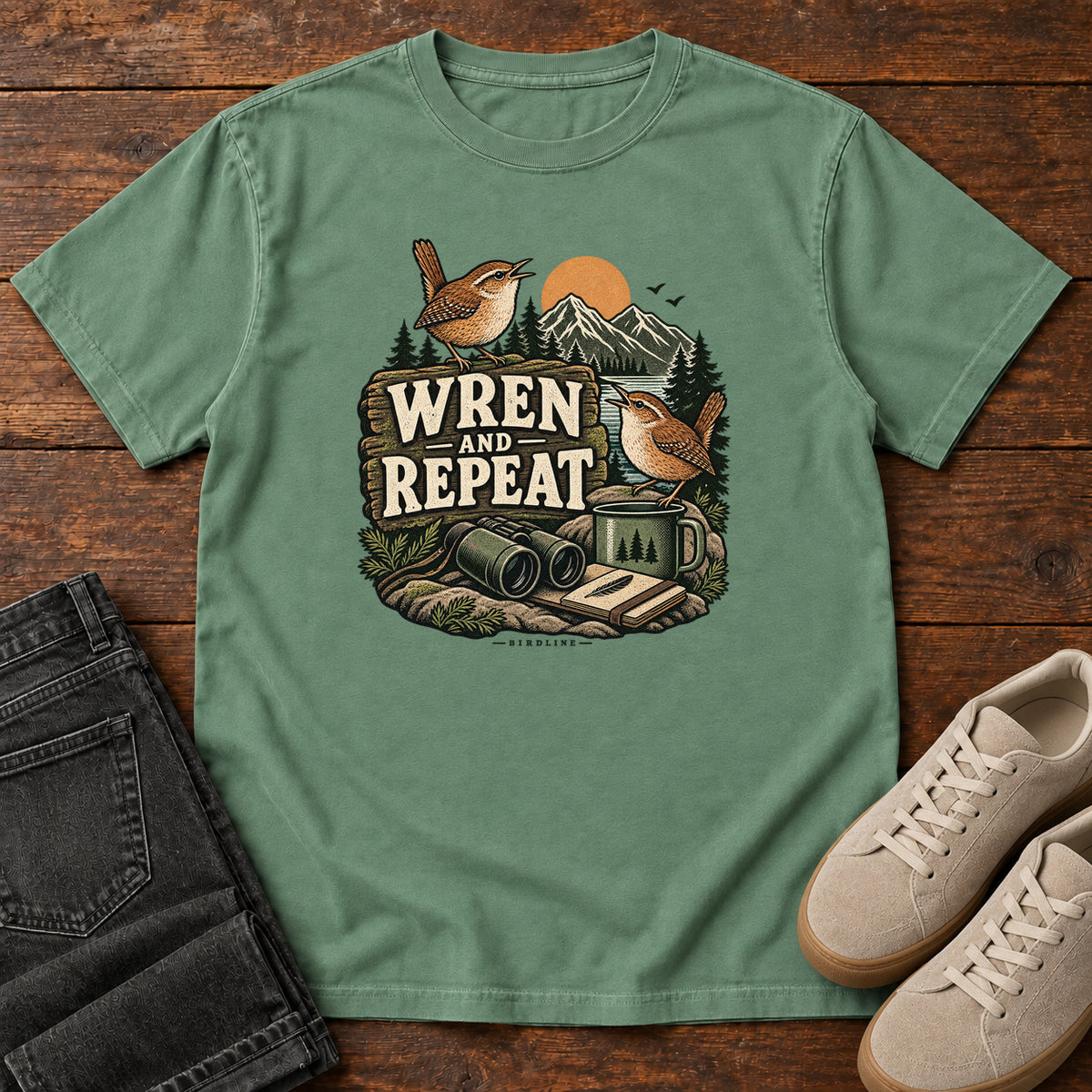 Light Green Wren and Repeat T-Shirt with two small brown birds, binoculars and a camp mug around Wren and Repeat lettering, front flat lay on wood.