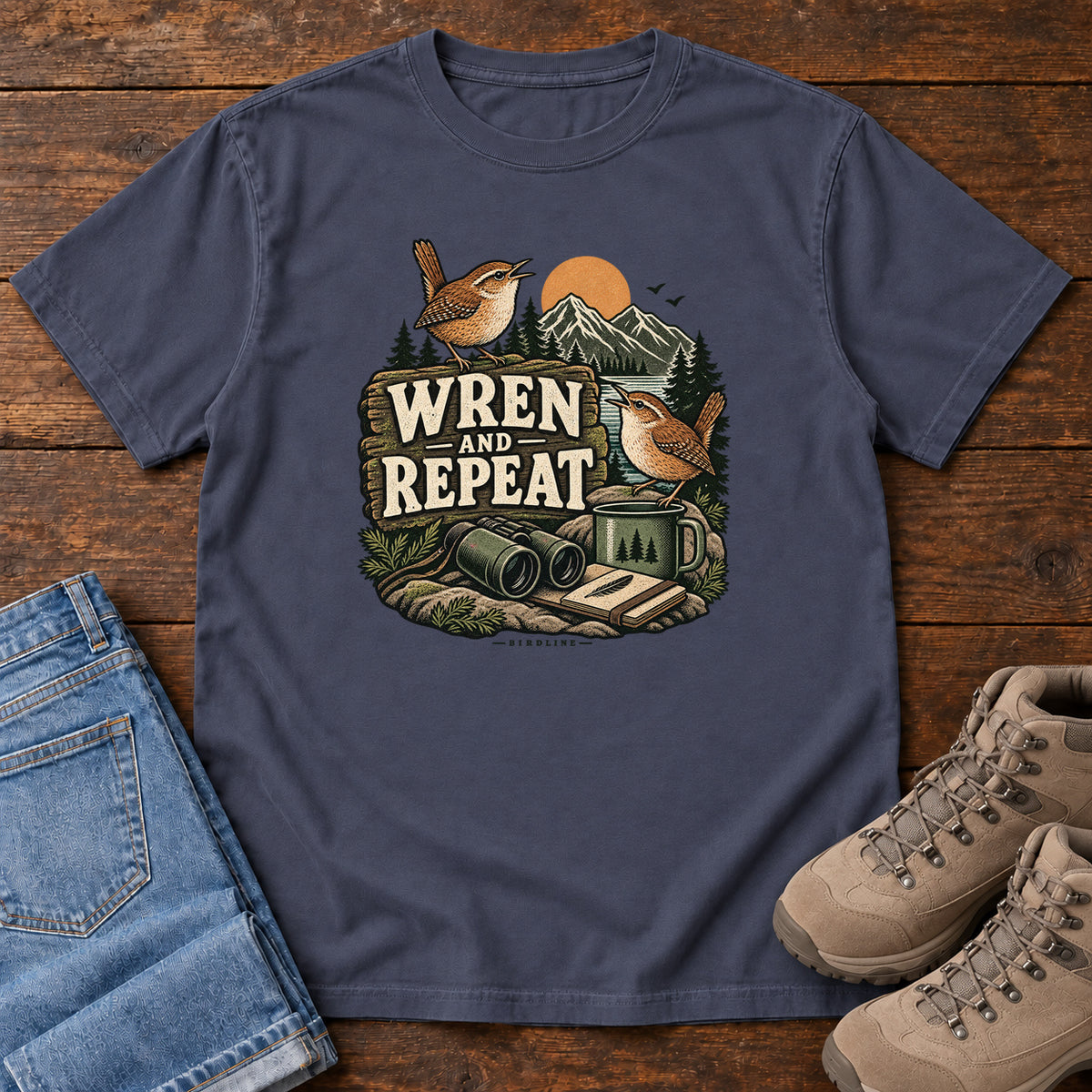Navy Wren and Repeat T-Shirt with two small brown birds, binoculars and a camp mug around Wren and Repeat lettering, front flat lay on wood.