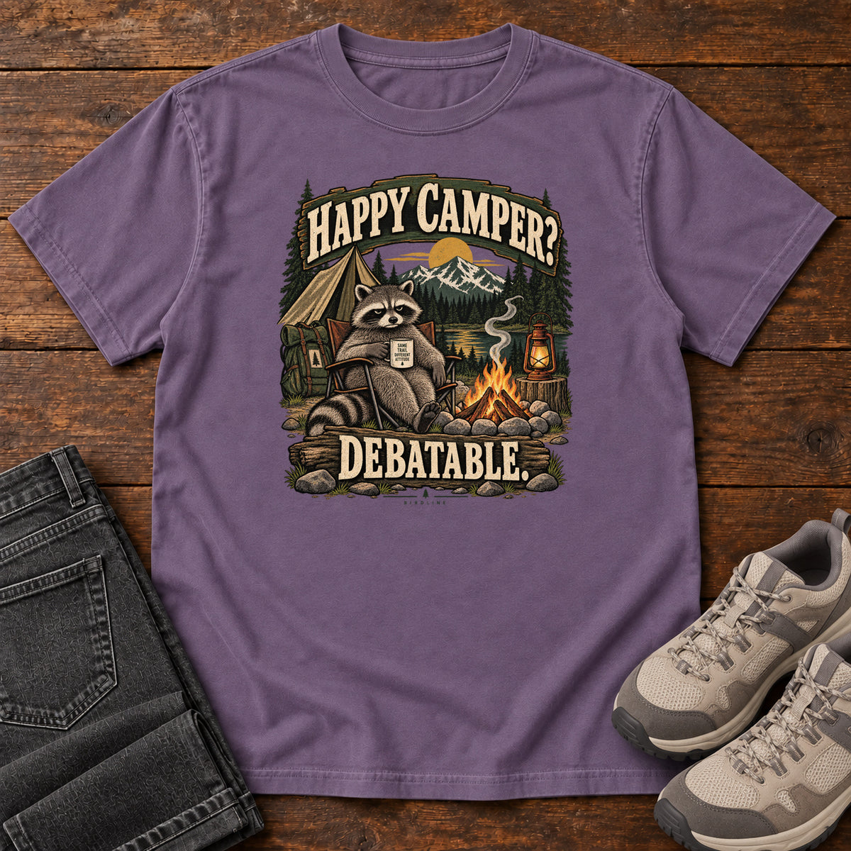 Grape Happy Camper Debatable T-Shirt with a raccoon holding a mug beside a campfire, tent and lantern, front flat lay on wood.