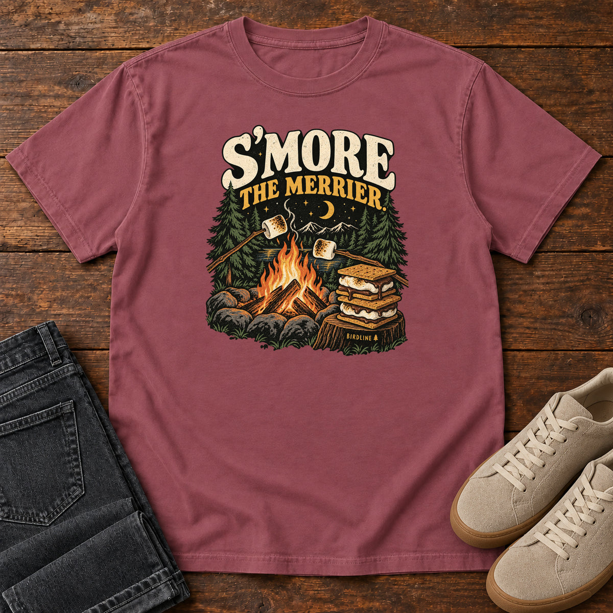 Brick Smore the Merrier T-Shirt with a campfire, marshmallows on sticks and stacked s’mores beneath a crescent moon; front flat lay on wood.
