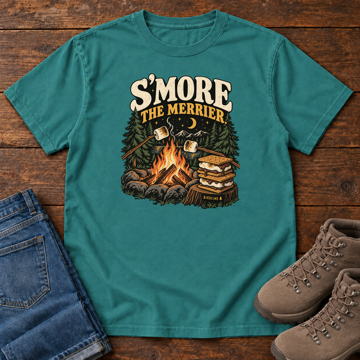 Emerald Smore the Merrier T-Shirt with a campfire, marshmallows on sticks and stacked s’mores beneath a crescent moon; front flat lay on wood.