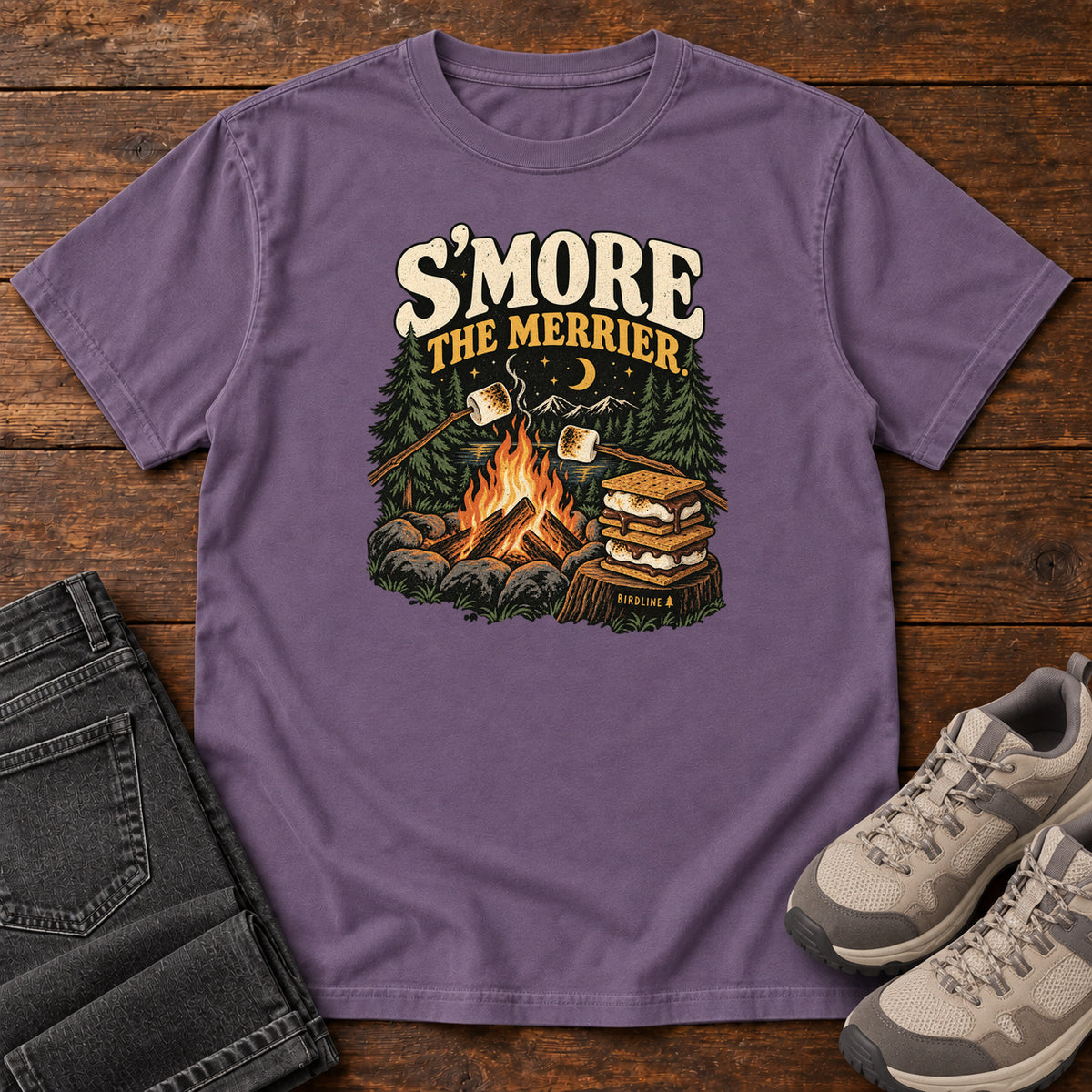 Grape Smore the Merrier T-Shirt with a campfire, marshmallows on sticks and stacked s’mores beneath a crescent moon; front flat lay on wood.