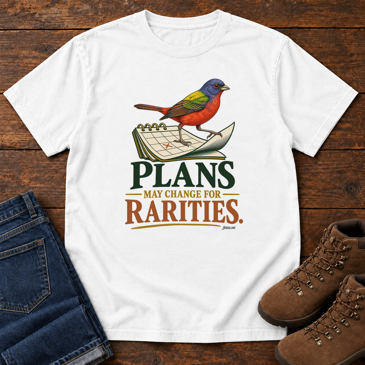 White Plans May Change for Rarities T-Shirt with a red, blue and green bird perched on a curled calendar page; front flat lay on wood.
