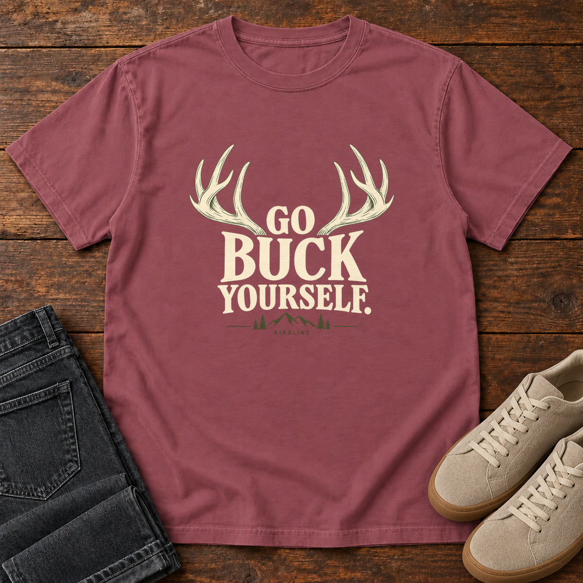 Brick Go Buck Yourself T-Shirt with cream deer antlers framing Go Buck Yourself lettering, front flat lay on wood.