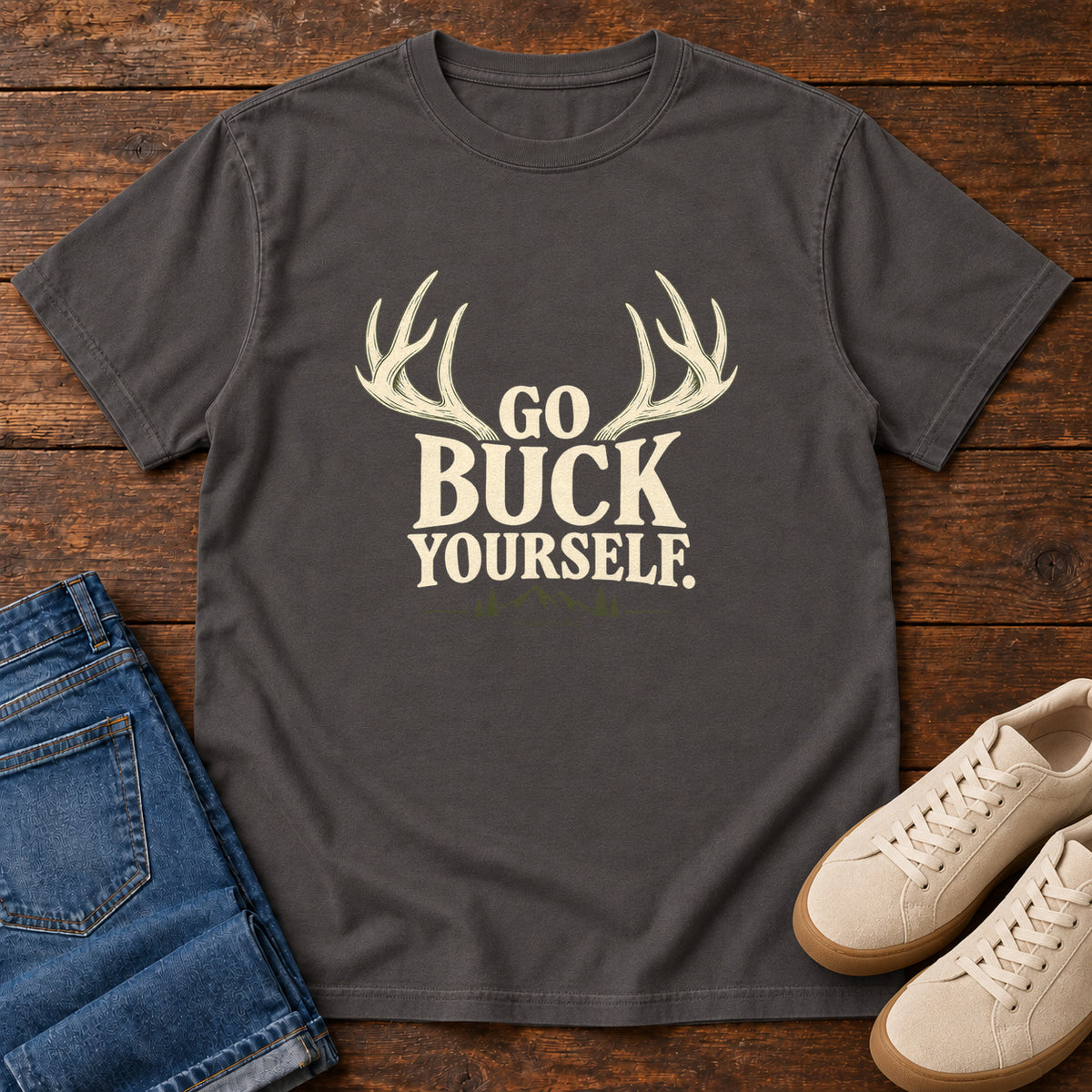 Graphite Go Buck Yourself T-Shirt with cream deer antlers framing Go Buck Yourself lettering, front flat lay on wood.
