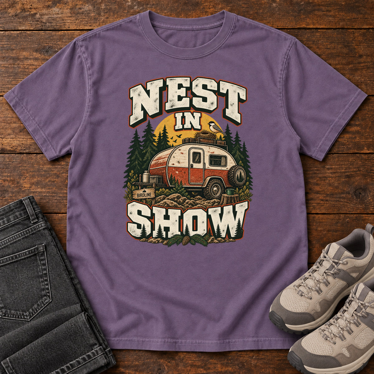 Grape Nest in Show T-Shirt with a red-and-cream camper beneath pines, with a small bird and nest on its roof; front flat lay on wood.