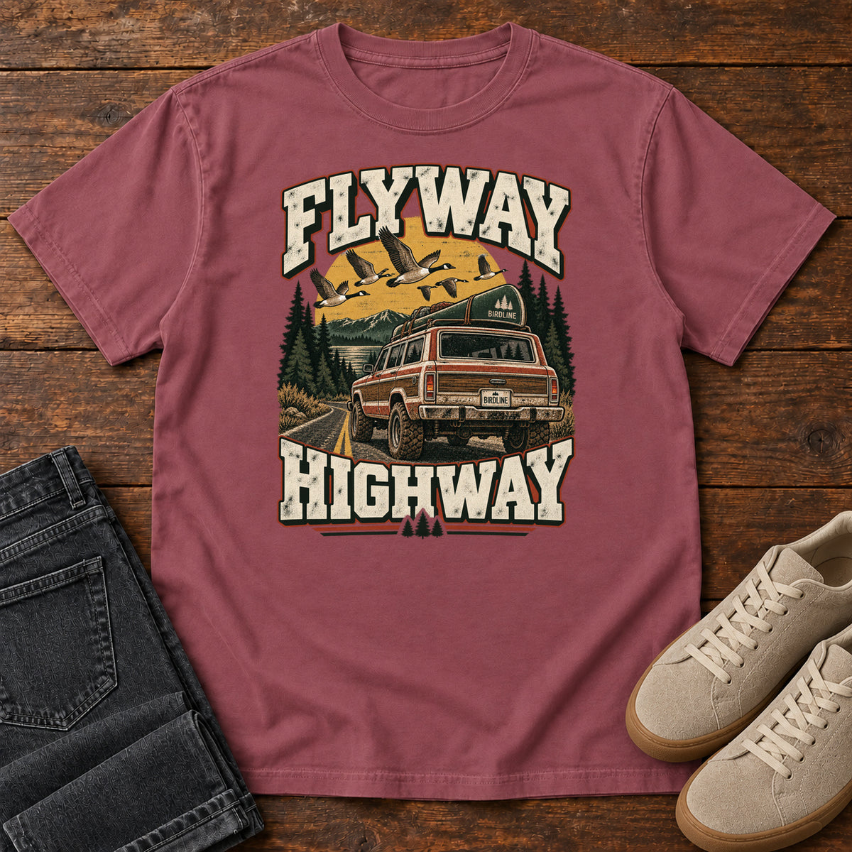 Brick Flyway Highway T-Shirt with a vintage pickup on a forest road with flying birds overhead; front flat lay on wood.