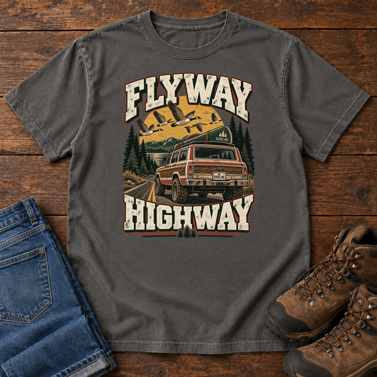 Pepper Flyway Highway T-Shirt with a vintage pickup on a forest road with flying birds overhead; front flat lay on wood.
