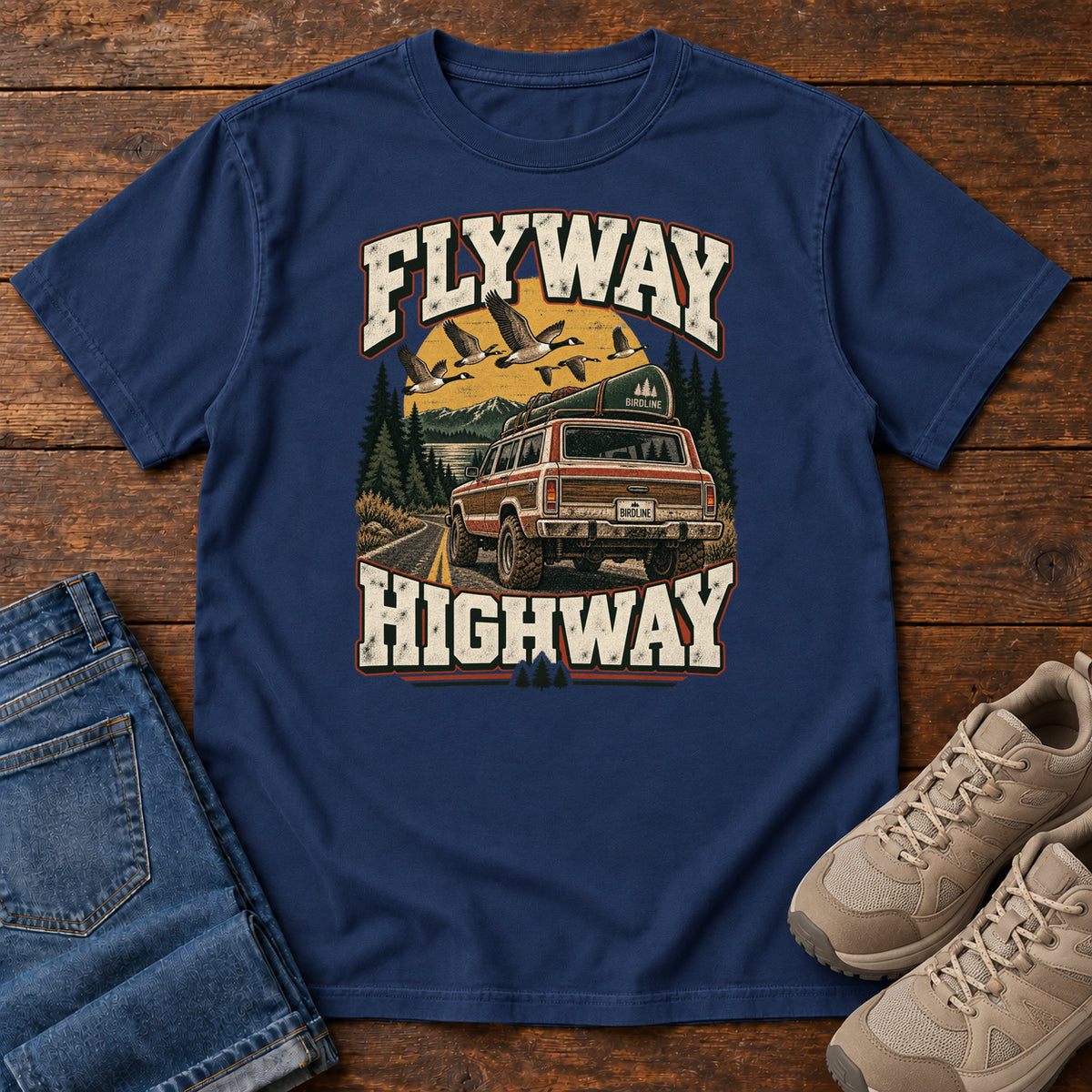 True Navy Flyway Highway T-Shirt with a vintage pickup on a forest road with flying birds overhead; front flat lay on wood.