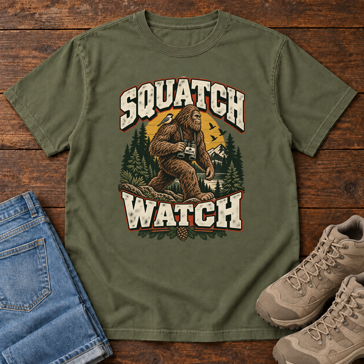 Squatch Watch T-Shirt in Hemp, front laid flat on wood, featuring a walking Sasquatch holding binoculars among pine trees, framed by large cream lettering.