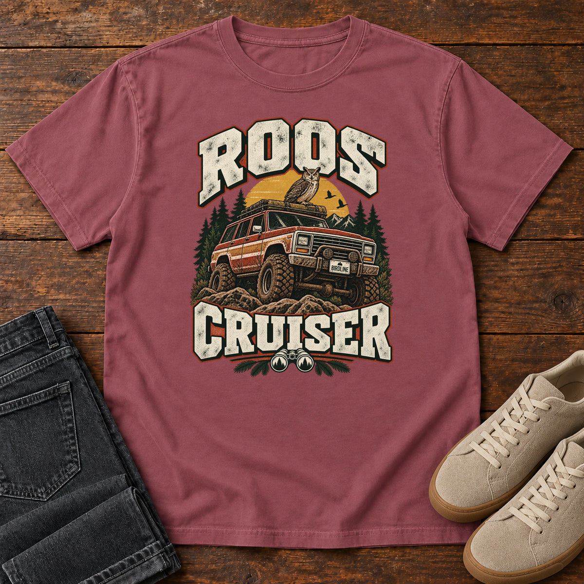 Brick Roos Cruiser T-Shirt with a bird perched on an off-road vehicle between distressed cream Roos Cruiser lettering, front flat lay on wood.