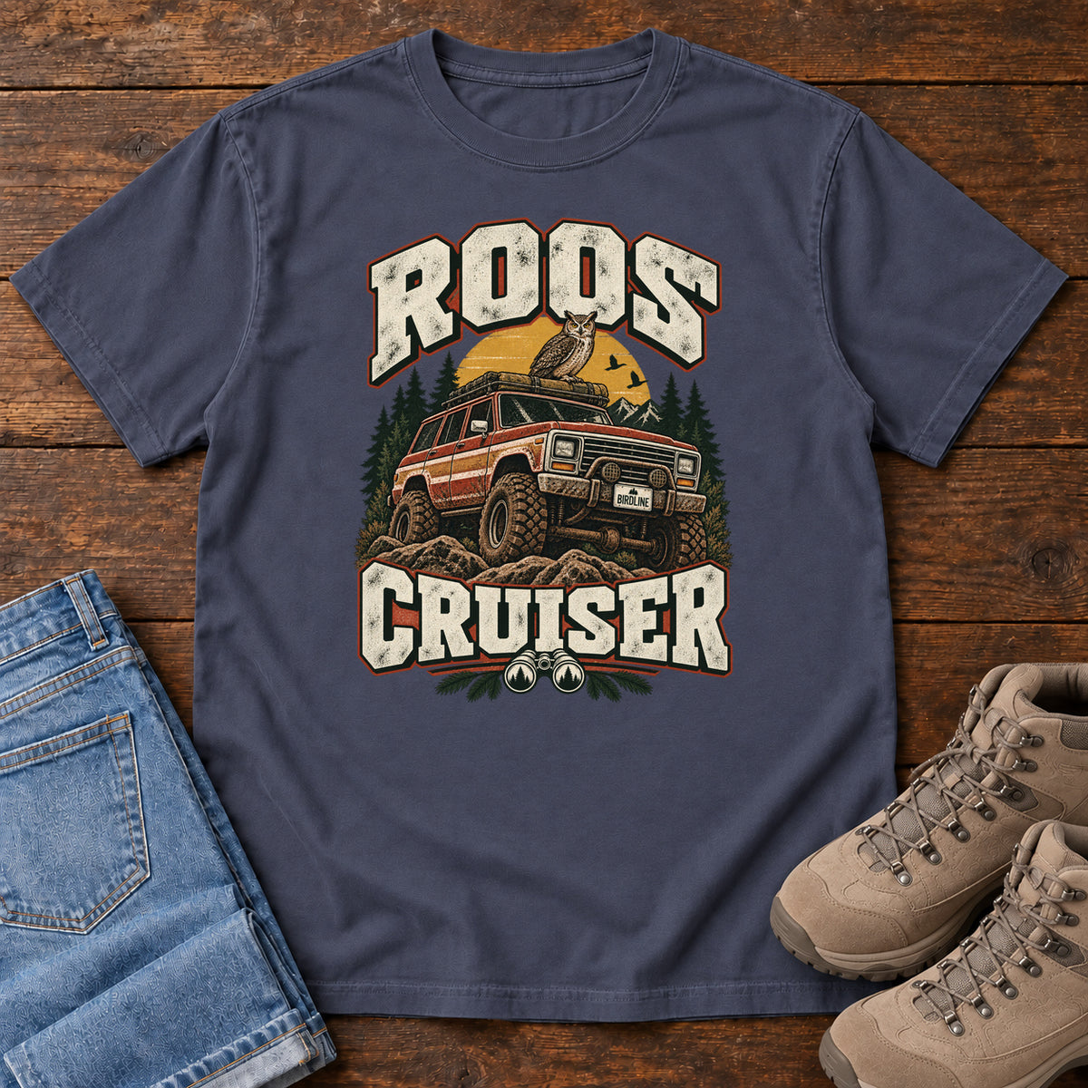 Navy Roos Cruiser T-Shirt with a bird perched on an off-road vehicle between distressed cream Roos Cruiser lettering, front flat lay on wood.