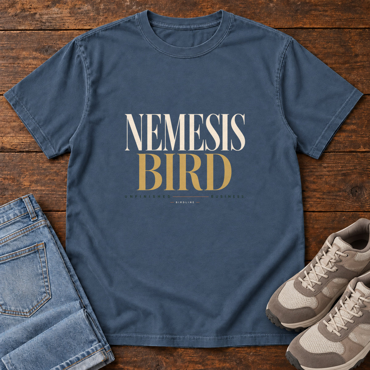 Midnight Nemesis Bird T-Shirt with cream-and-gold serif lettering, front flat lay on wood.