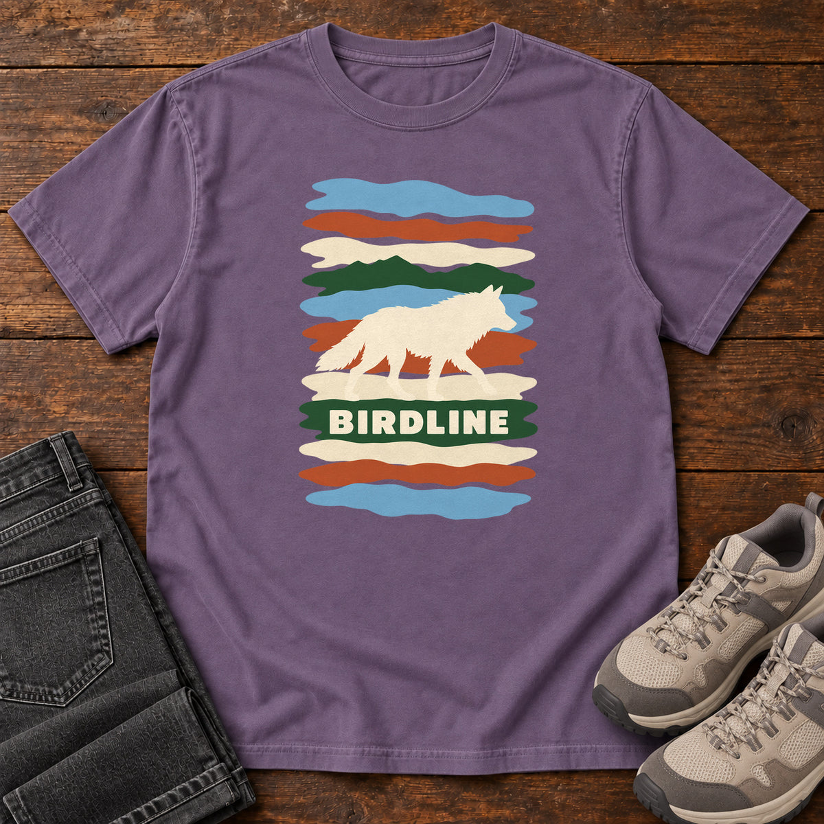 Grape Birdline White Wolf Stripes T-Shirt with a cream wolf silhouette over colorful wavy stripes and Birdline lettering; front flat lay on wood.