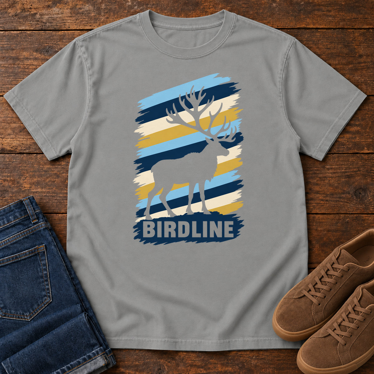 Birdline Elk Stripes T-Shirt in Grey, front laid flat on wood, featuring an elk silhouette against blue, cream and gold brushstroke stripes above BIRDLINE lettering.